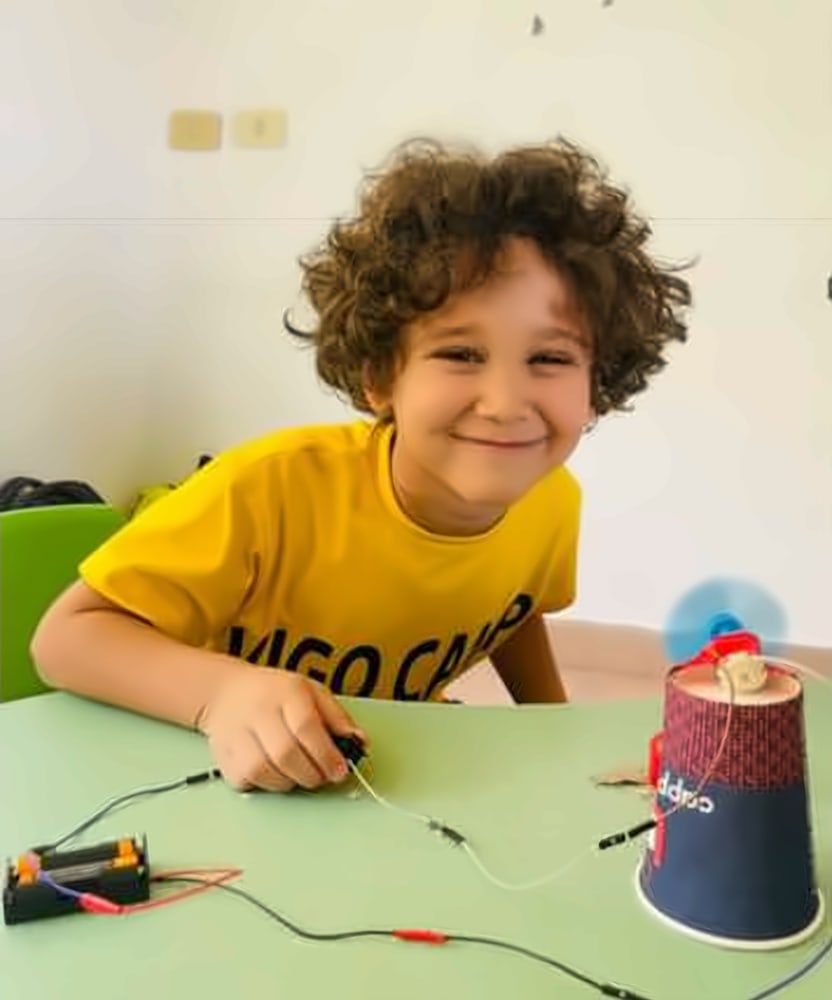A smiling boy building a little electric fan at Vigo Camp