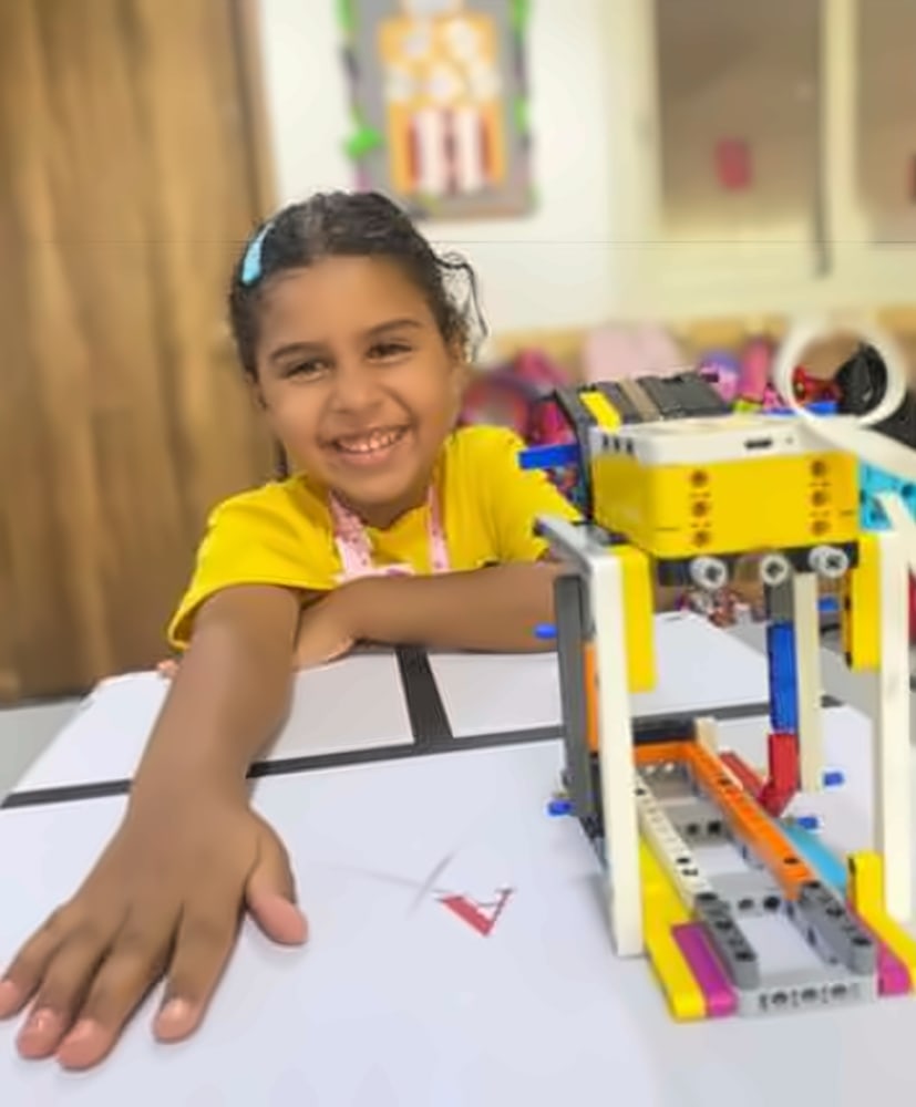 A girl smiling next to the robot she built